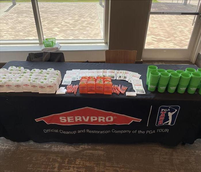 a table with a black SERVPRO table cloth, green cups, brochures, and personal restoration kits on it. 