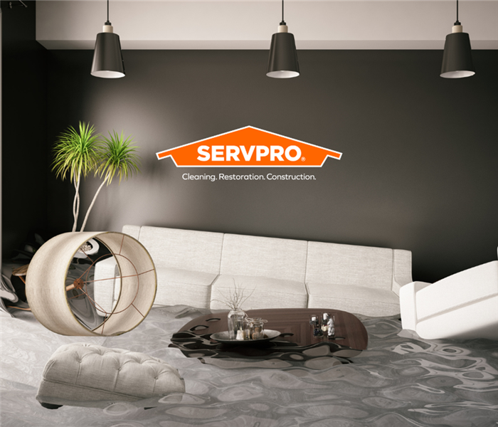 Living room flooded with water and a SERVPRO logo with subtext that says cleaning. restoration. construction
